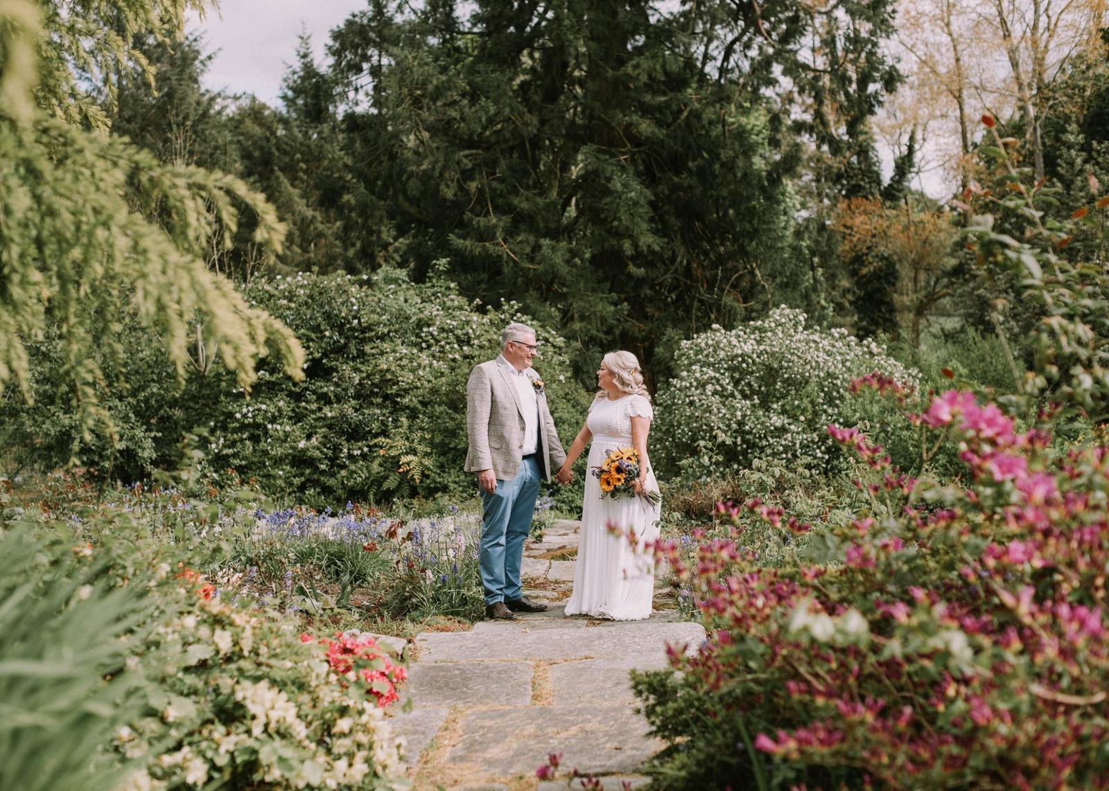 Bride and groom holding hands on the stone path between the flower borders at Dunmore Gardens