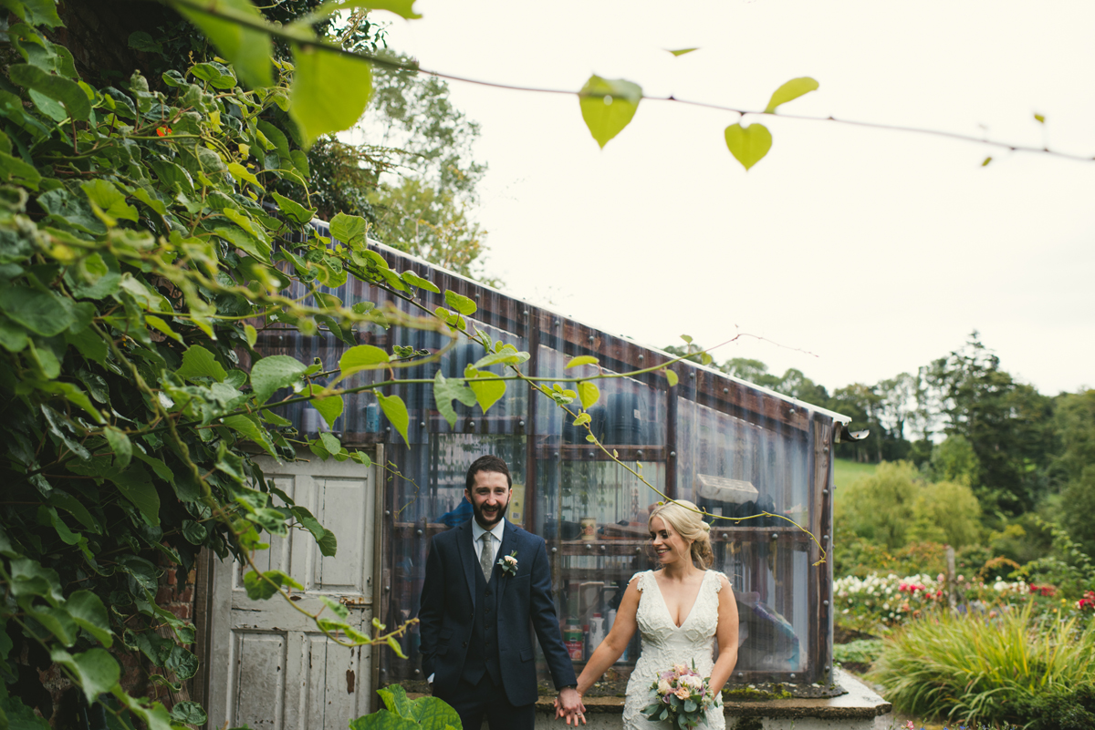 Bride and groom walking hand in hand past the ivy-clad glasshouse in the walled garden