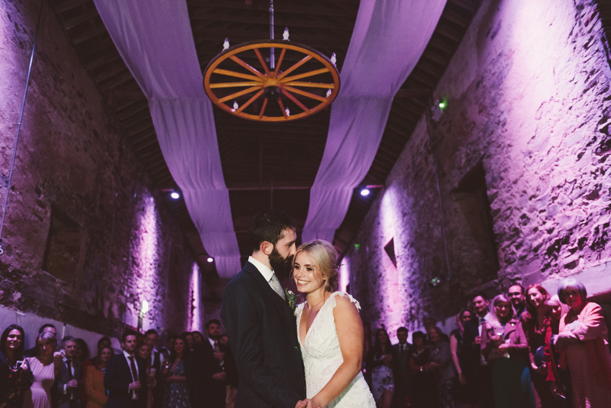First dance in the stone barn beneath the cartwheel chandelier and violet uplighting
