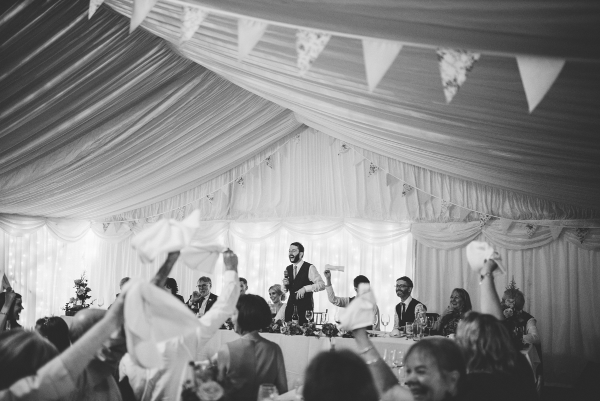 Guests raising napkins during the speeches in the draped marquee