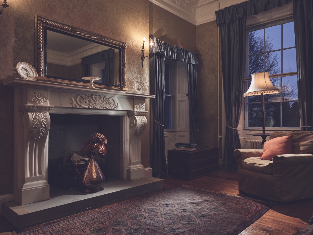 The drawing room at Dunmore House, with marble fireplace, lamplight and evening windows